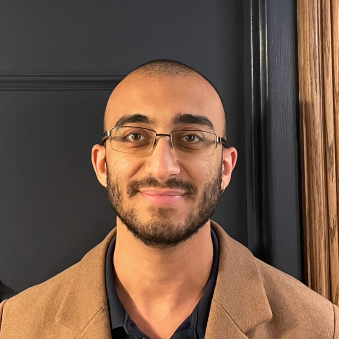 Man wearing a brown coat and glasses indoors